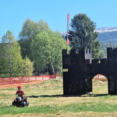 Barnfyrhjuling på bana med stort svart slott och fjäll i bakgrundnen